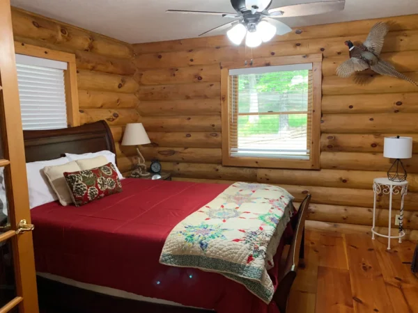 A bedroom with a bed, ceiling fan and wood walls.