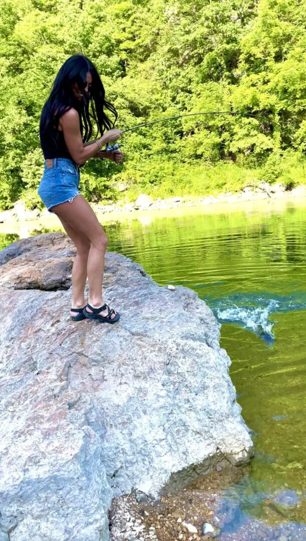 A woman standing on top of a rock near water.