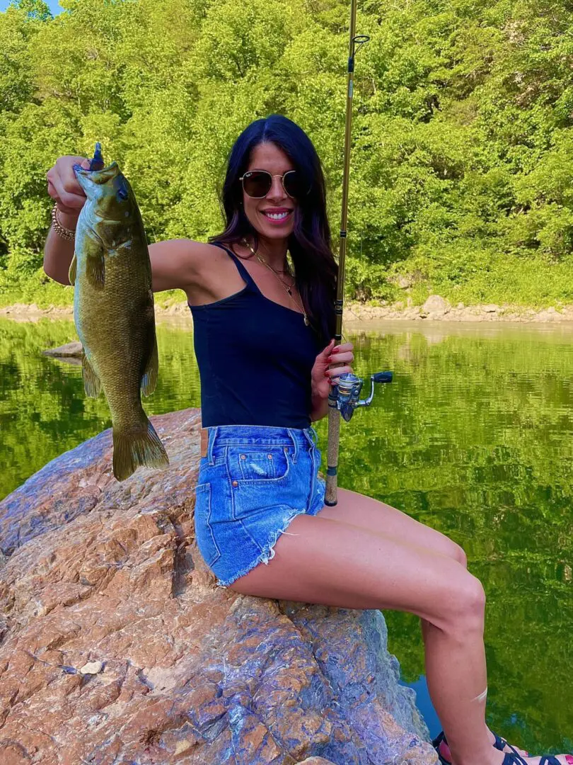 A woman holding a fish while sitting on rocks.