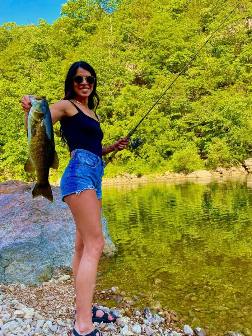 A woman holding a fish while standing on rocks.