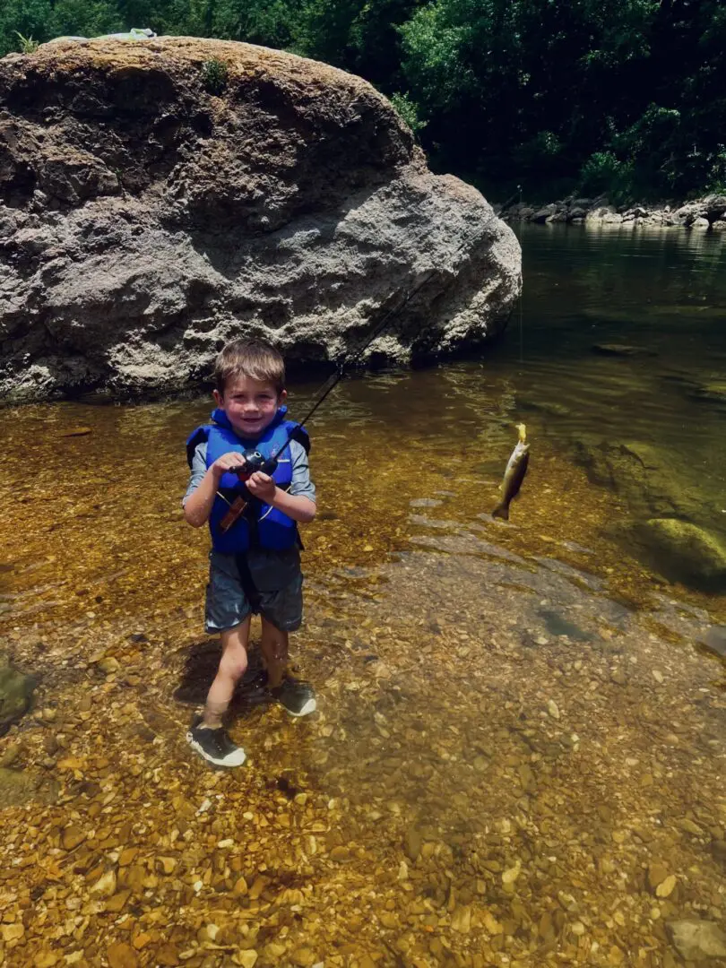 A boy standing in shallow water near rocks.