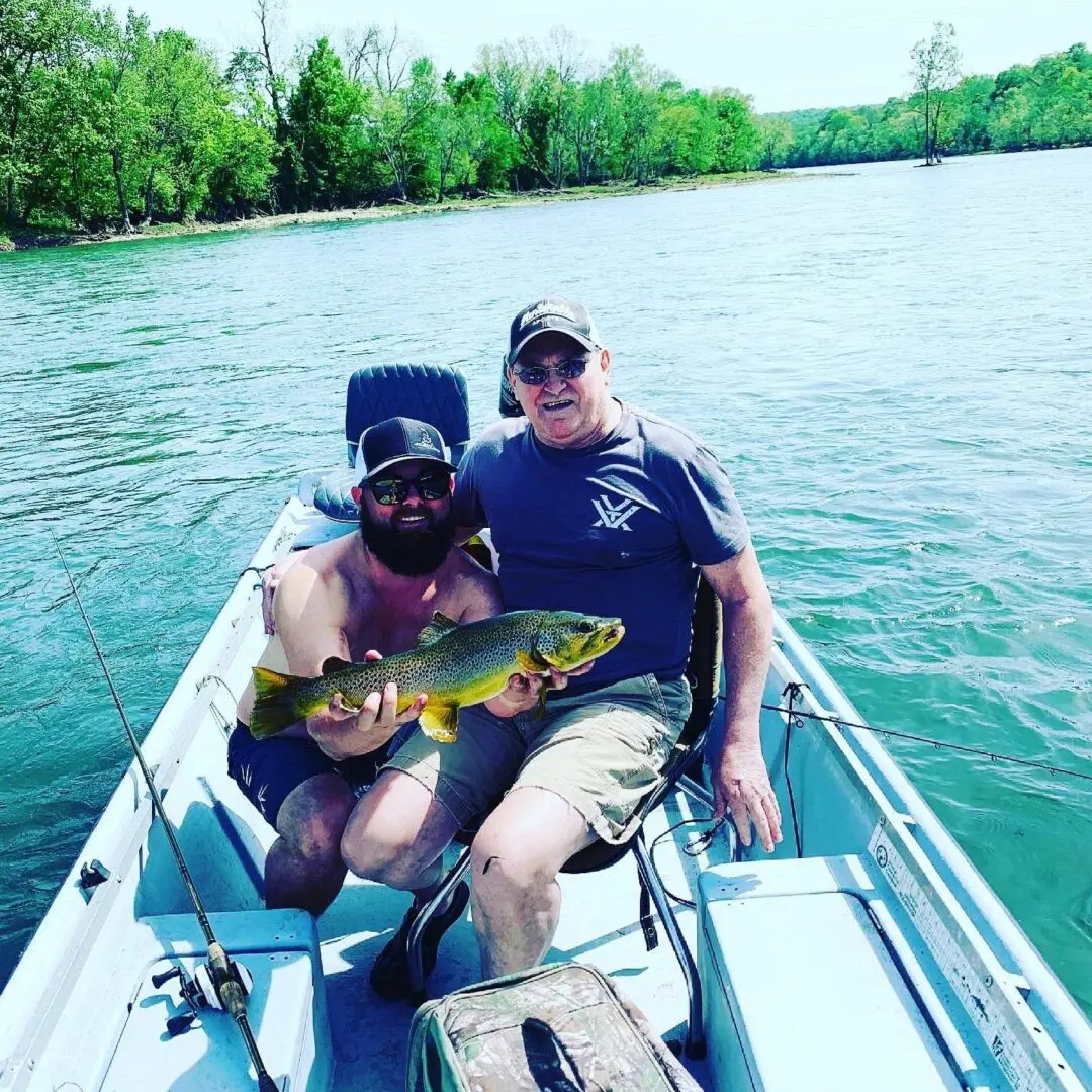 Two men sitting on a boat holding fish.