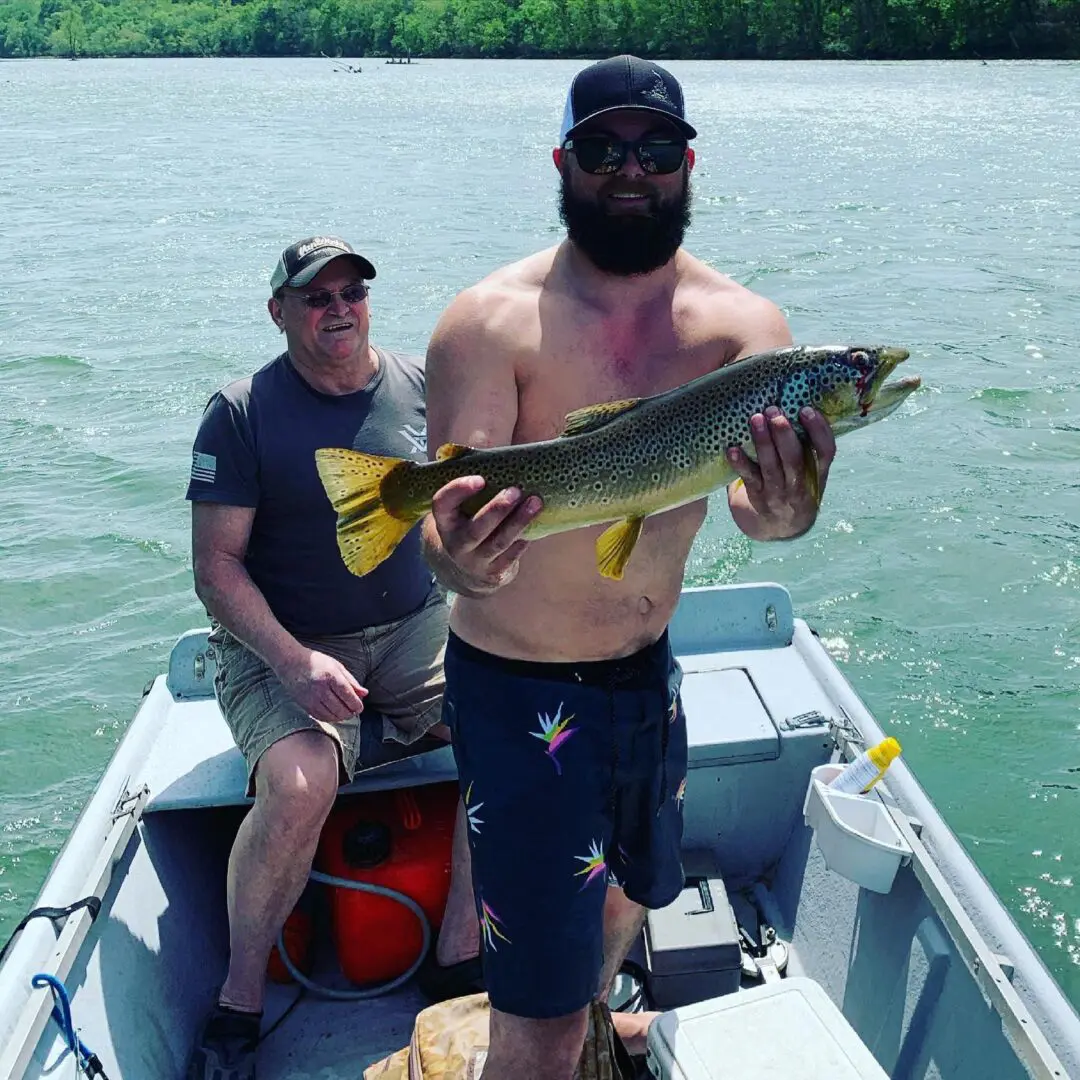 A man holding a fish while sitting on the back of a boat.