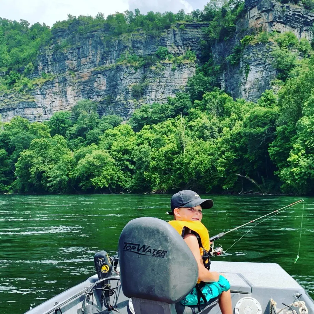 A man fishing on the water with trees in the background.